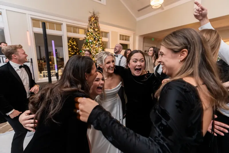 Friends laugh and embrace Ashley in a cream-colored ballroom decorated with a golden Christmas tree.