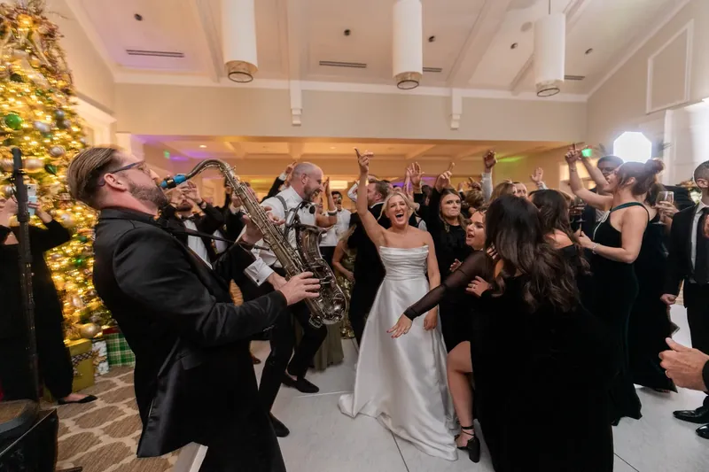 Ashley dances with guests in a white dress while a saxophonist plays at the reception.