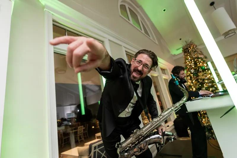A saxophonist in a tuxedo plays energetically during the reception, arm raised mid-performance.