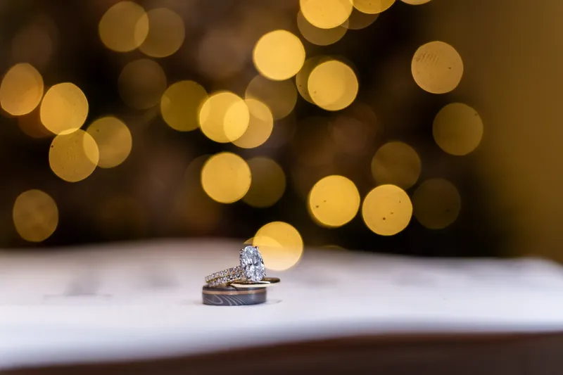 Wedding rings rest on white fabric with warm golden bokeh lights in the soft-focus background.