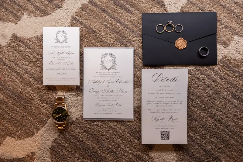 Wedding rings, invitations, and a black envelope with wax seal arranged on a textured beige surface.