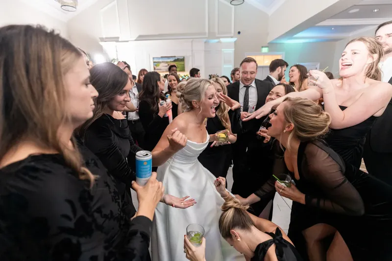Ashley in her white wedding dress smiles while dancing with guests in black and white formal wear.