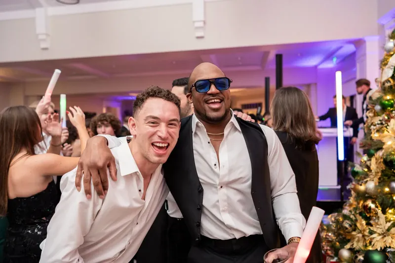 Two men in white shirts and sunglasses grin while dancing at the reception.