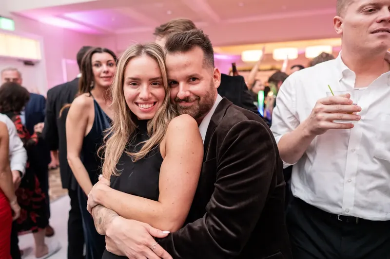Ashley and Craig embrace in the ballroom as pink uplighting washes the reception space behind them.
