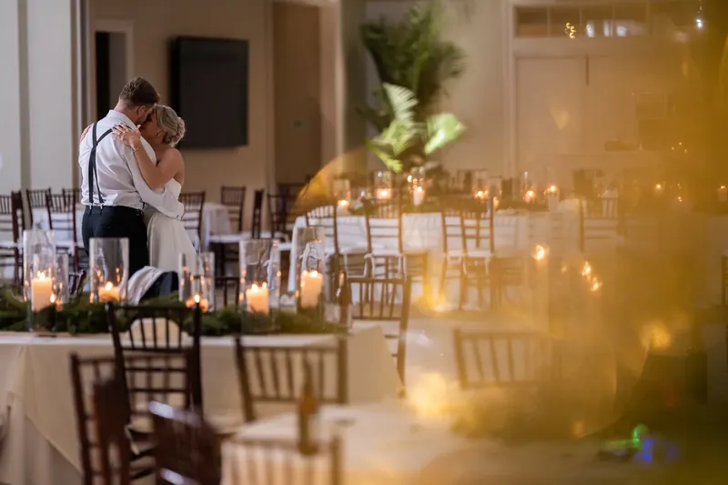 Ashley and Craig share a close moment near glass doors with candlelit tables arranged throughout the ballroom.