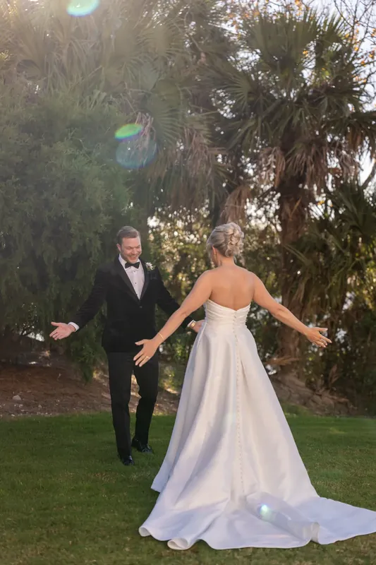 Craig and Ashley walk on a manicured lawn with towering palms at Sawgrass Marriott, her white gown's train flowing behind.