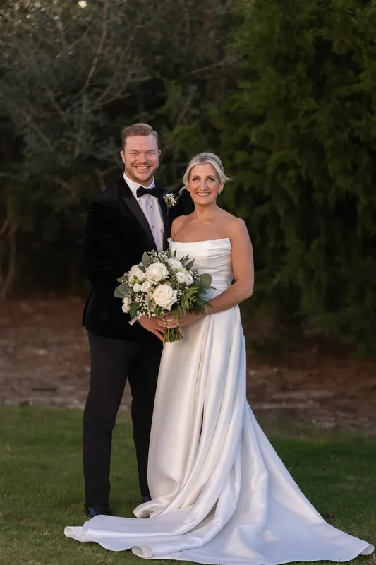 Craig and Ashley stand together on the grounds, his arm around her as she holds her white bridal bouquet.