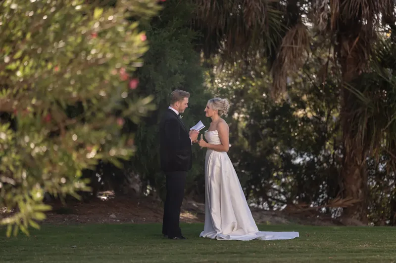 Craig holds Ashley's hand while she gazes at him beneath towering trees at the resort.