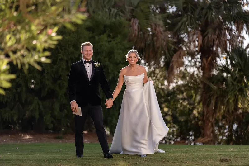 Ashley and Craig walk hand in hand across the manicured lawn with Spanish moss-draped trees framing the scene.