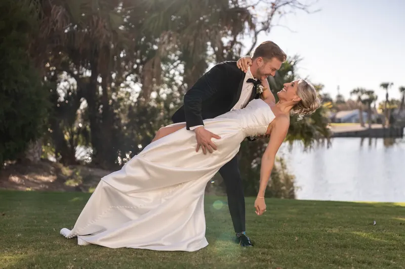 Craig dips Ashley low for a kiss with a pond and palm trees visible behind them.