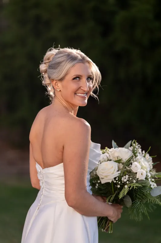 Ashley smiles over her shoulder holding a white and green bouquet in her strapless gown.
