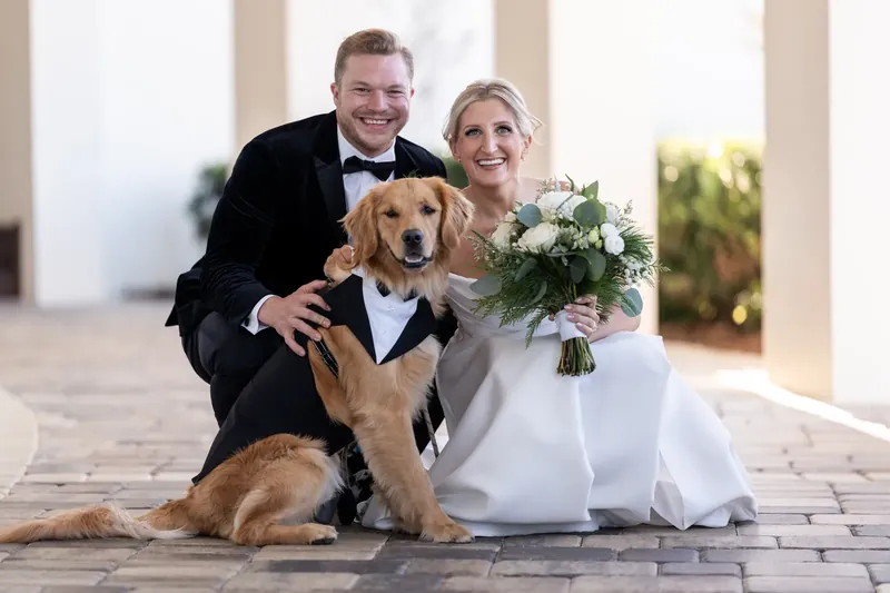Craig and Ashley kneel beside their golden retriever on the stone terrace, smiling at the camera.