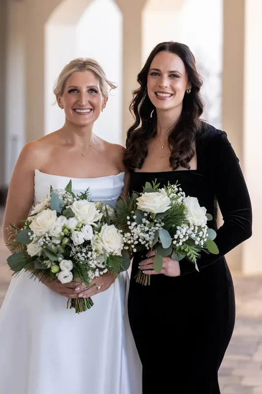 Ashley and a companion hold white and green bouquets while standing beneath arched columns at the resort.