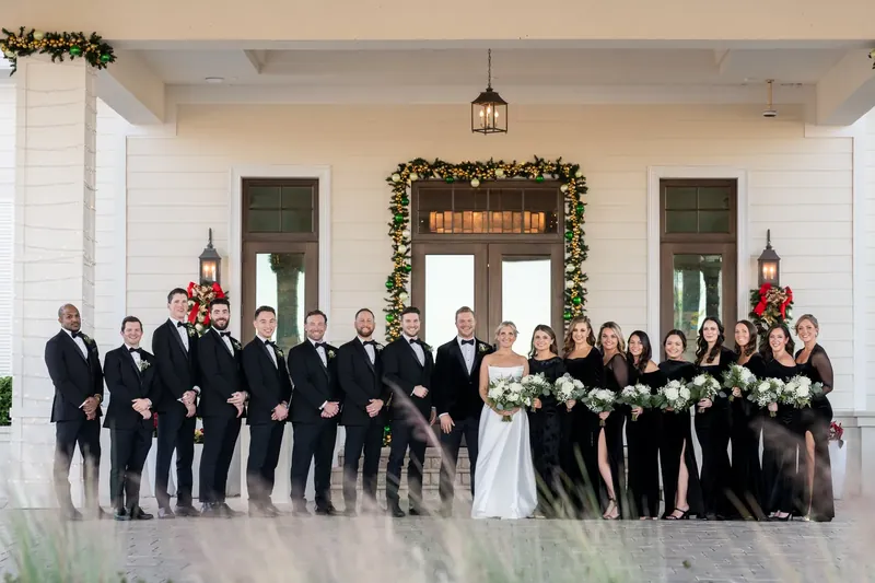 The full wedding party lines up in front of the venue's grand entrance, decorated with garland and lanterns.
