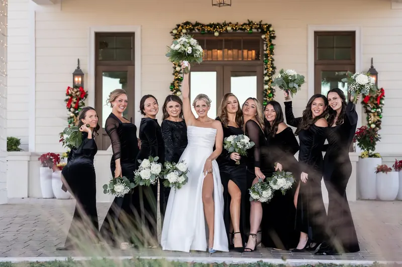 Ashley stands center with attendants on either side, all holding white bouquets in front of the festive entrance.