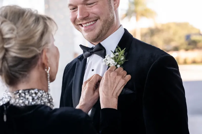 Ashley fastens Craig's boutonniere as he grins at the resort venue.
