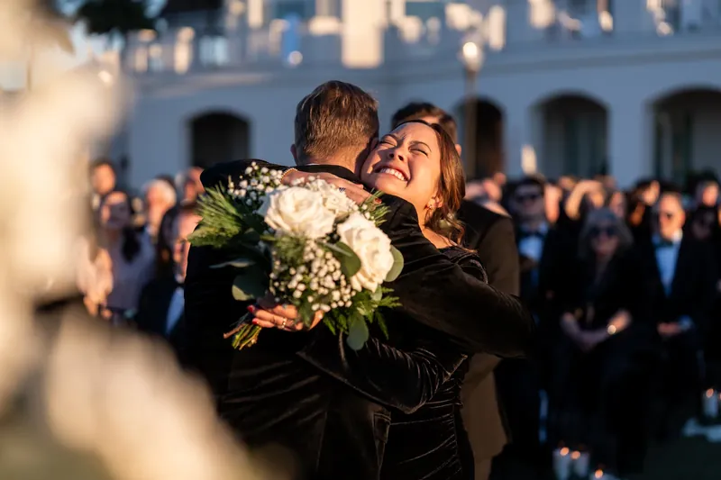 Craig embraces Ashley joyfully after their first kiss as a married couple, surrounded by guests.