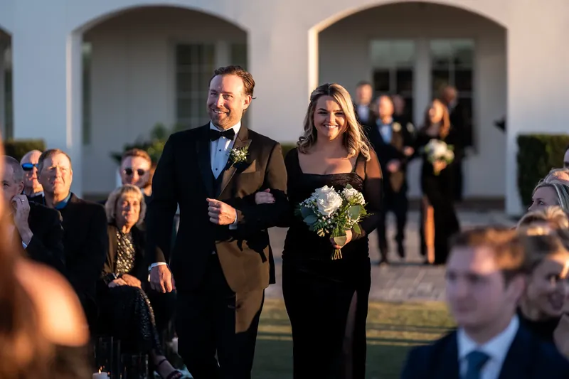 Ashley and Craig stroll together down the aisle following their ceremony, smiling at well-wishers.