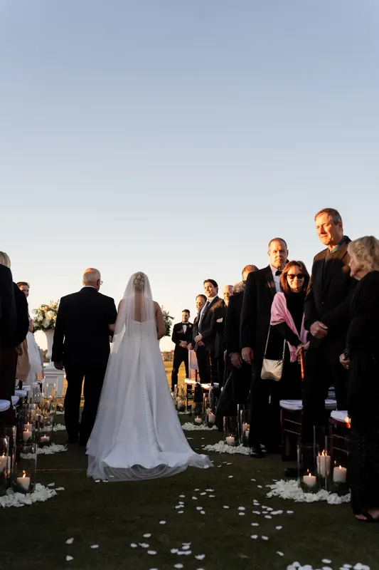Craig stands facing Ashley across the grass aisle during their outdoor ceremony as guests gather in rows on either side.