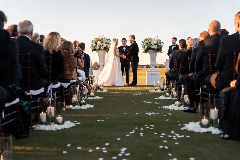 Guests seated along a petal-lined aisle watch Ashley and Craig exchange vows on the golf course.