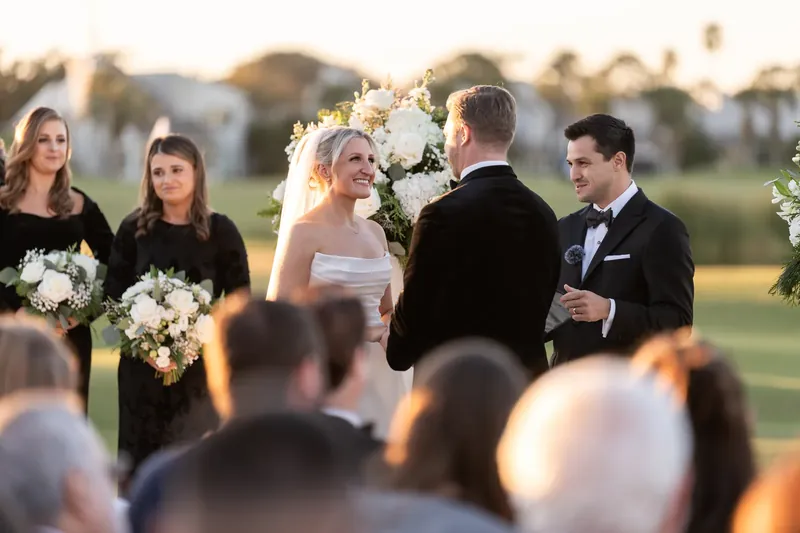 Ashley in white and Craig in dark suit stand at the altar with attendants holding bouquets nearby.