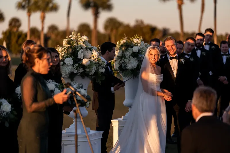 Ashley in her white dress walks the recessional past glowing white florals as guests line the aisle.