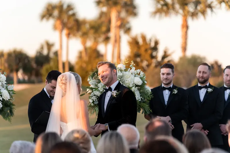 Craig stands at the altar with groomsmen flanking him and palm trees lining the golf course behind.