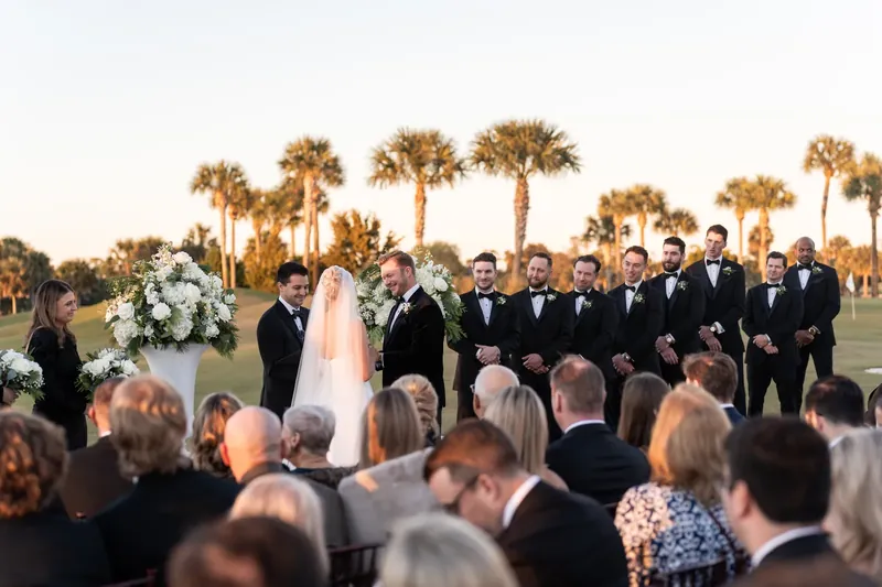 The couple exchanges vows before guests seated along the fairway with palmetto trees in the distance.