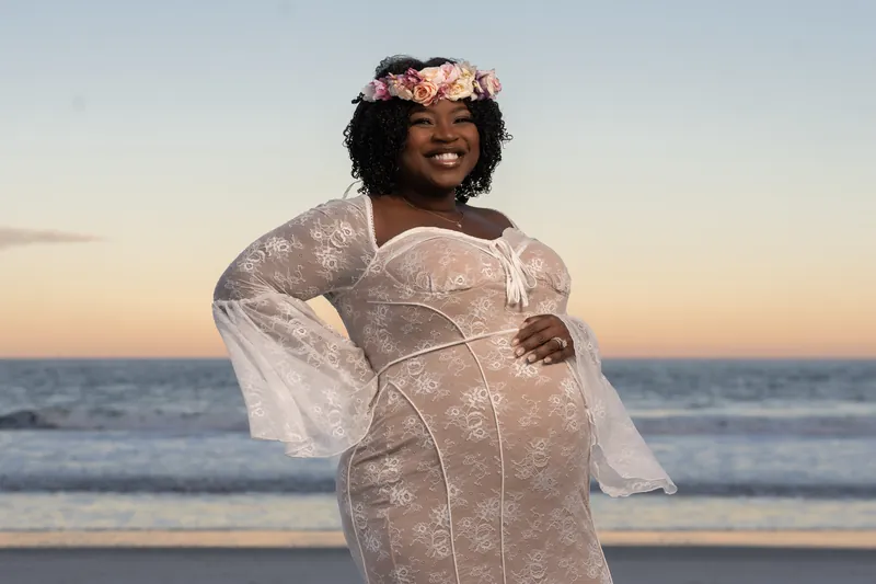 Ashley wears a sheer lace wrap and floral crown while smiling at sunset at Vilano Beach, St. Augustine.