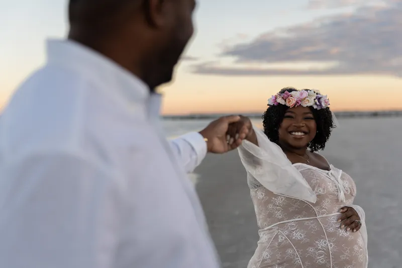JB reaches toward Ashley's face as she laughs, both dressed in white at Vilano Beach at dusk.