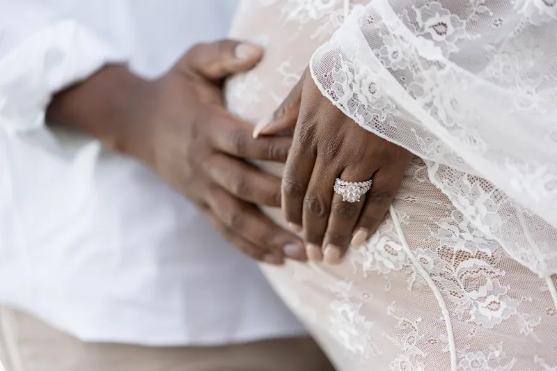 Detail shot of couple's hands cradling baby bump, showing engagement ring