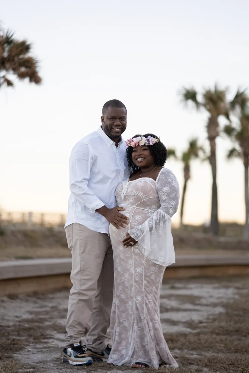Ashley and JB standing together, his hand on her bump, palm trees behind