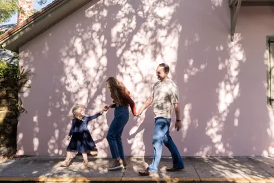 Family walking along sidewalk with tree shadows on pink wall in downtown St. Augustine