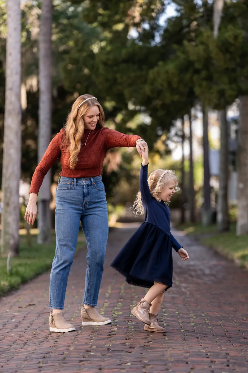 Ashley walks hand-in-hand with their daughter down a tree-lined brick path in Downtown St Augustine, both smiling