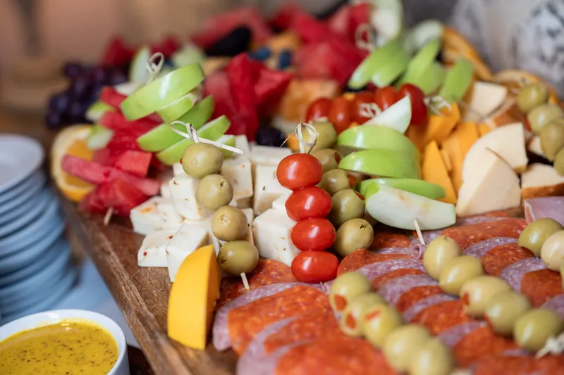 Charcuterie board overflowing with cured meats, cheese, olives, grapes, and fresh vegetables arranged on a wooden platter.