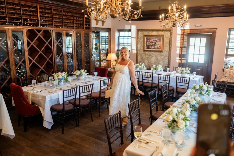 Ashley stands in an elegant white dress amid the dining room, with guest tables and floral arrangements visible throughout