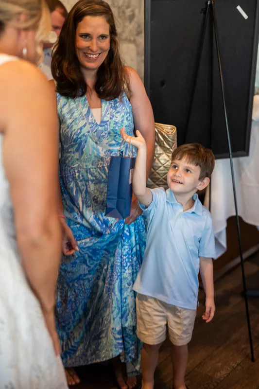 A woman in a blue patterned dress smiles while talking with a young boy in a light blue button-up shirt.