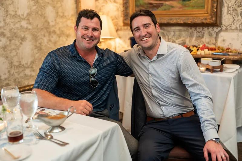 Two men smile at a white-draped table at The Chatsworth Pub and Tea Room, with drinks and place settings visible.