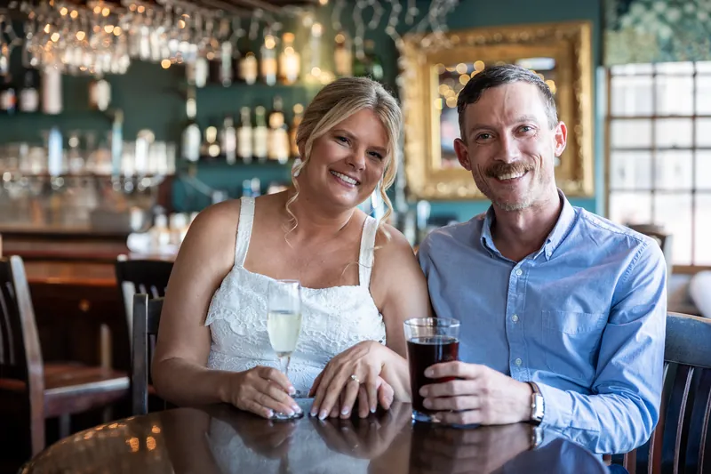 Ashley and Jared sit at the bar at The Chatsworth Pub and Tea Room, holding drinks and laughing together.
