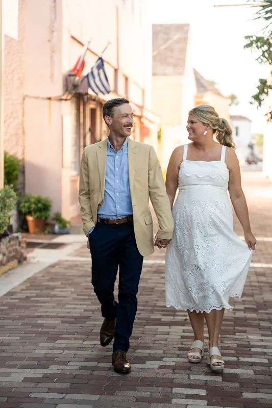 Ashley and Jared hold hands while walking past colorful storefronts along a brick street in Downtown St Augustine.