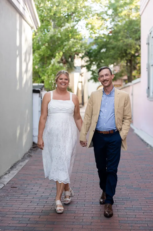 Ashley and Jared walk hand in hand down a brick-lined alley in Downtown St Augustine, with green foliage and historic