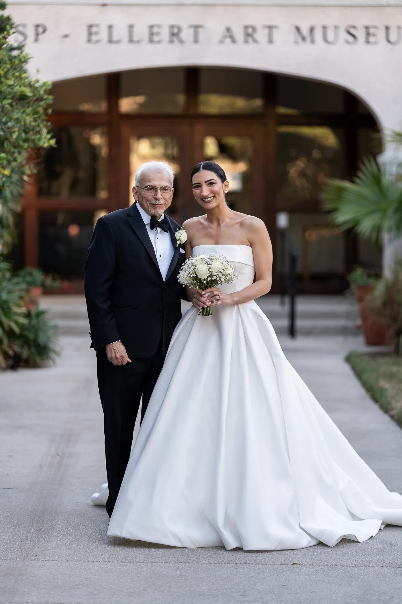 Bride and elderly man posing outside Ellert Art Museum entrance on wedding day