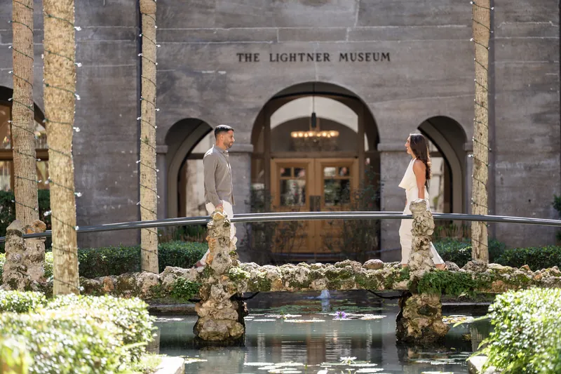 Beltran and Gabriela stand facing each other across the reflecting pool, holding hands at the museum courtyard.