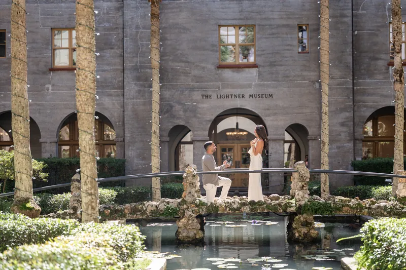 Two people embrace on a platform framed by flowering arrangements and ivy-covered columns at the Lightner Museum.