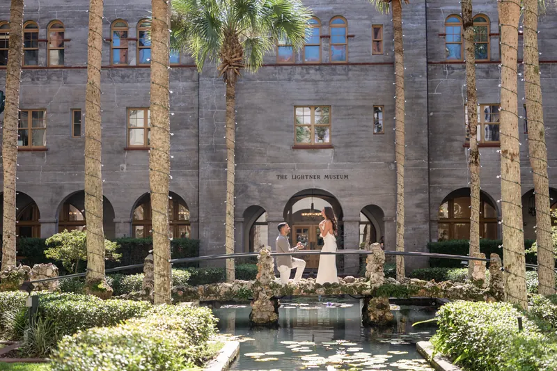 Beltran and Gabriela stand together on an ornate platform with white blooms, reflected in a pool below the museum's arched facade.