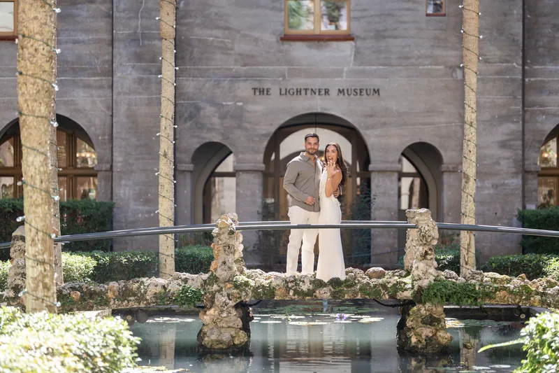 Two people face each other on a stone bridge beneath arched architecture, the museum's courtyard visible behind them.
