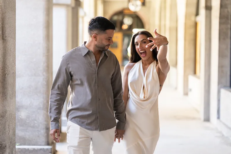 Two people walk side by side down a colonnaded corridor at the Lightner Museum, one wearing a gray shirt and the other in cream.