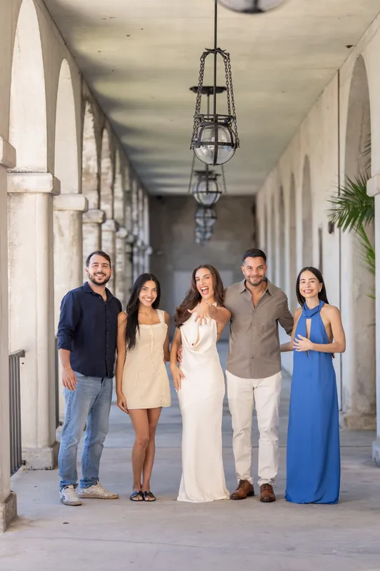 Five people, including someone in a white gown, stand together under a hanging lantern in the Lightner Museum's covered colonnade.