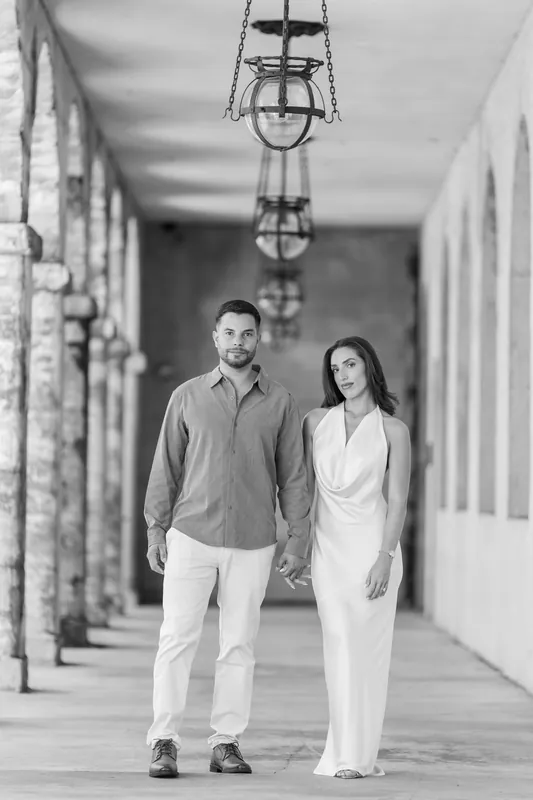 Beltran and Gabriela walk hand in hand through a colonnade at the Lightner Museum Courtyard, framed by hanging lanterns and classical arches.