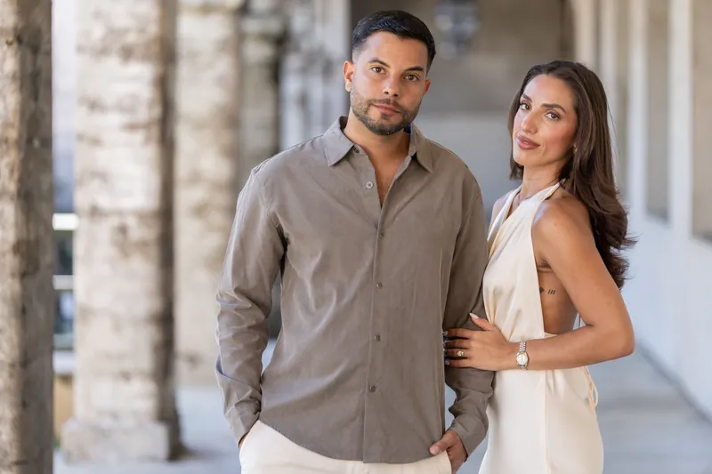 Two people stand together in the museum's covered corridor, one in a taupe shirt and one in a sleeveless cream top, looking toward each other.